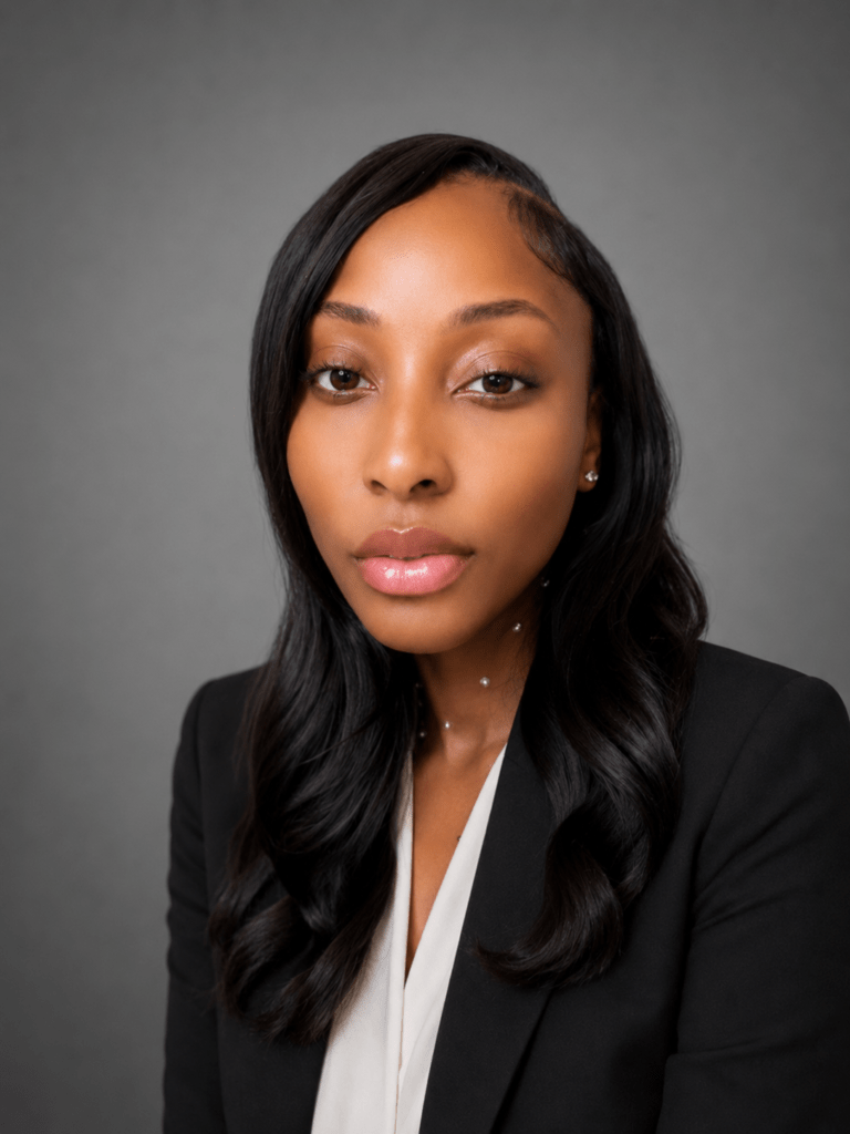 Head-and-shoulders professional black woman in a blazer and white blouse, looking at the camera against a gray studio background (corporate headshot).
