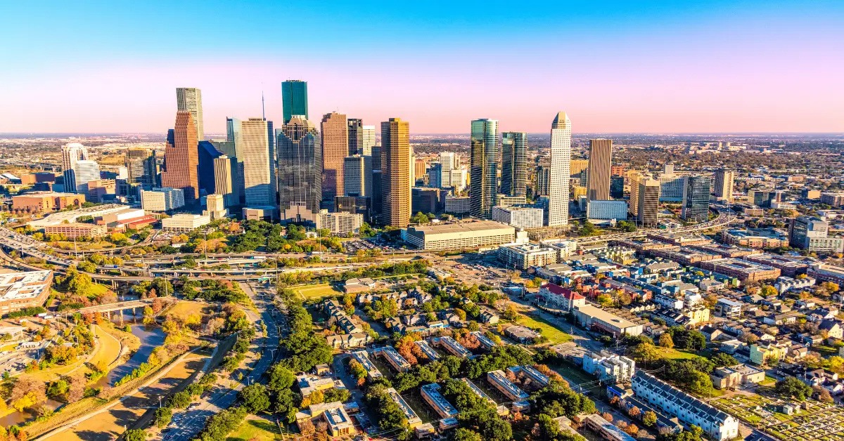 Aerial view of a downtown skyline with tall skyscrapers and a network of highways and residential blocks nearby.